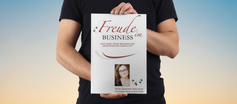 Person hält Buch "Freude im Business" vor sich, Hintergrund Himmel.