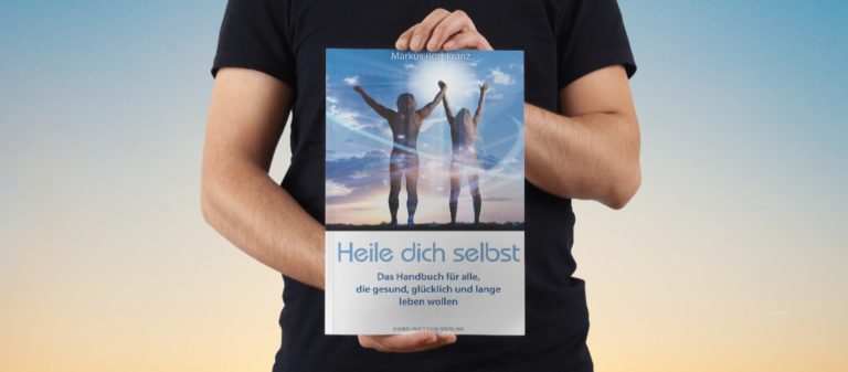 Person hält Buch "Heile dich selbst" gegen den Himmel, symbolisiert Selbstheilung.