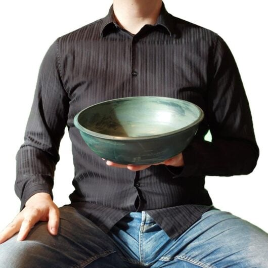 Energieschale-Groesse-gruen-schraeg Cooler Typ hält eine getöpferte grüne Schale in die Kamera