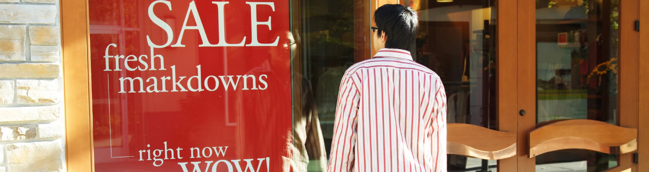 Person vor Schaufenster mit "SALE" und "fresh markdowns" Schildern.