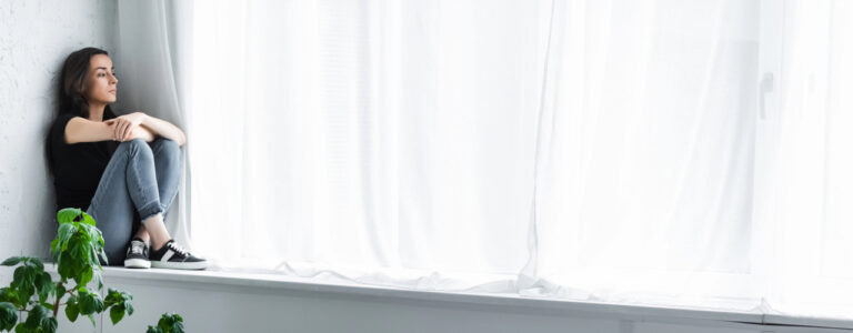 Nachdenkliche Frau sitzt am Fenster mit Blick nach draußen.